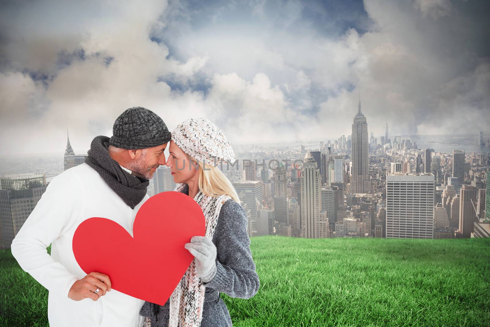 Smiling couple in winter fashion posing with heart shape against cloudy sky over city