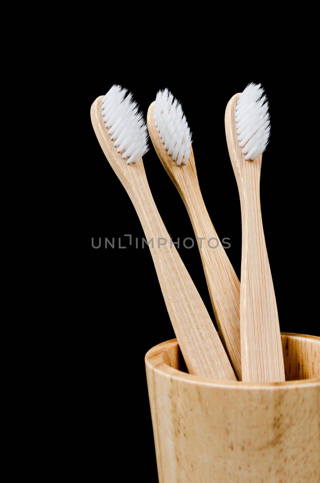 Bamboo toothbrushes in wooden cup on black background. by Gamjai