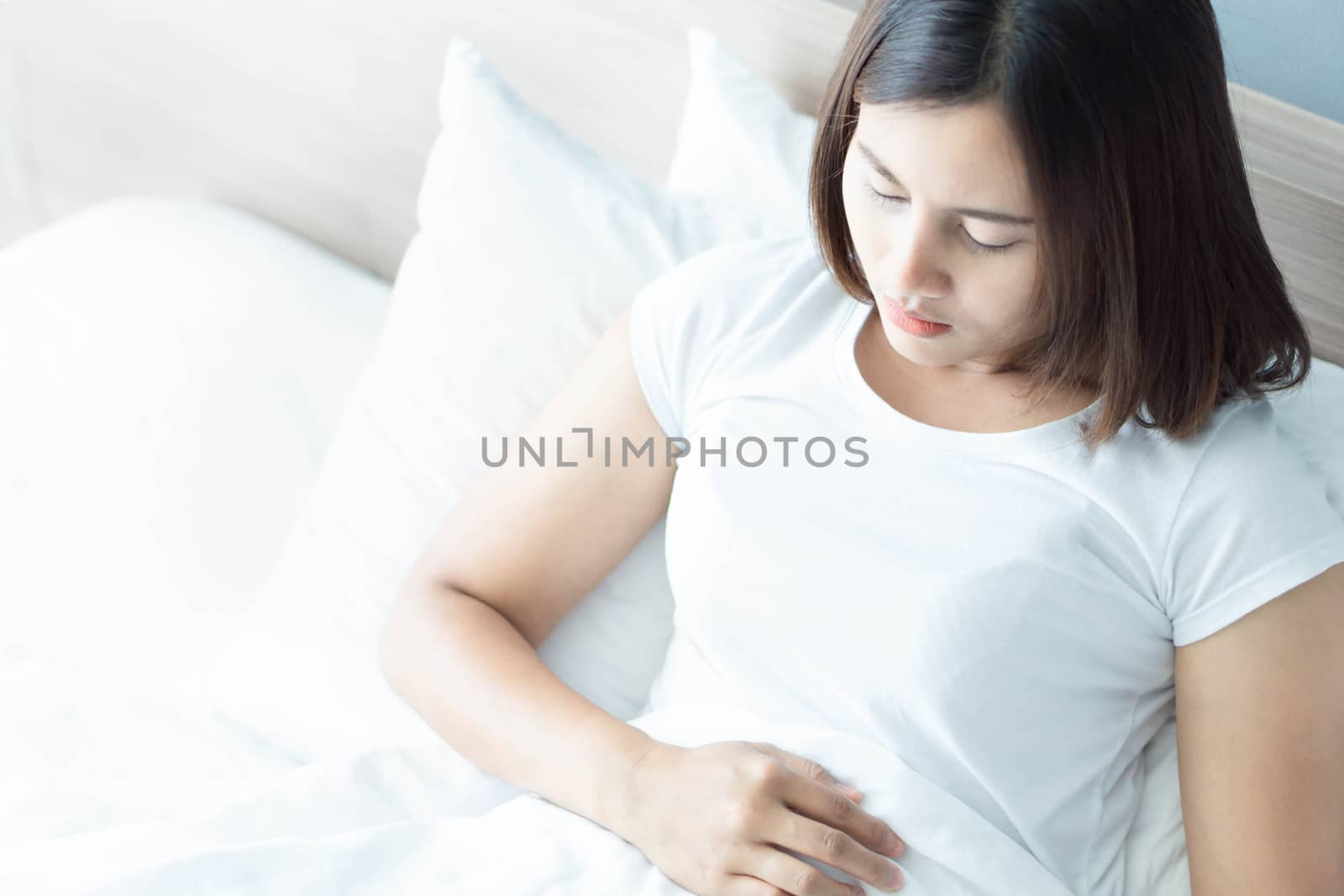 Close up woman stomachache lying on white bed, health care concept, selective focus