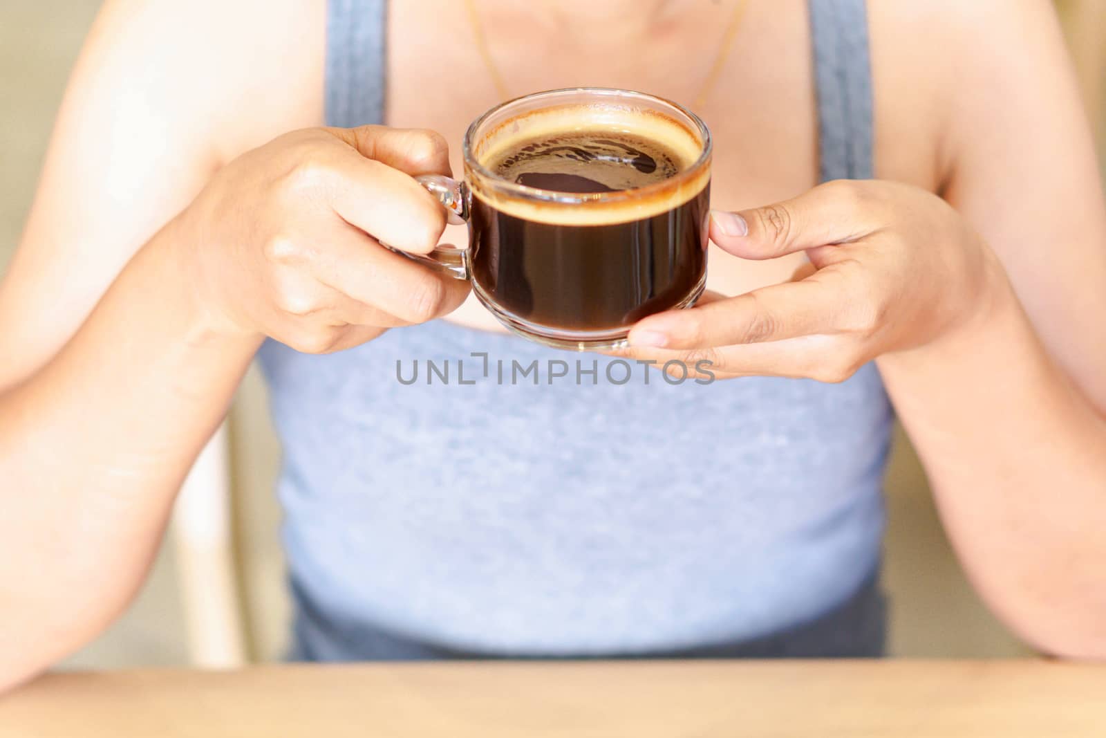 Closeup woman hand holding glass of hot americano coffee, selective focus, vintage tone