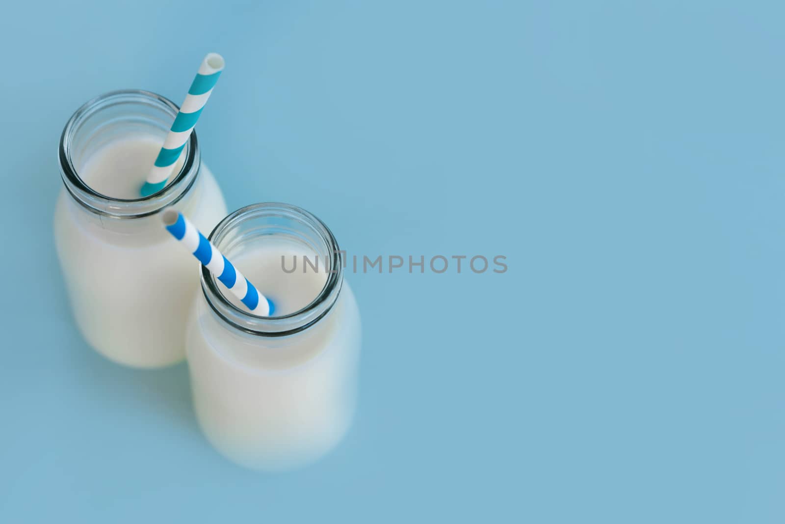 Bottle of fresh milk with straw on light blue background, food healthy concept