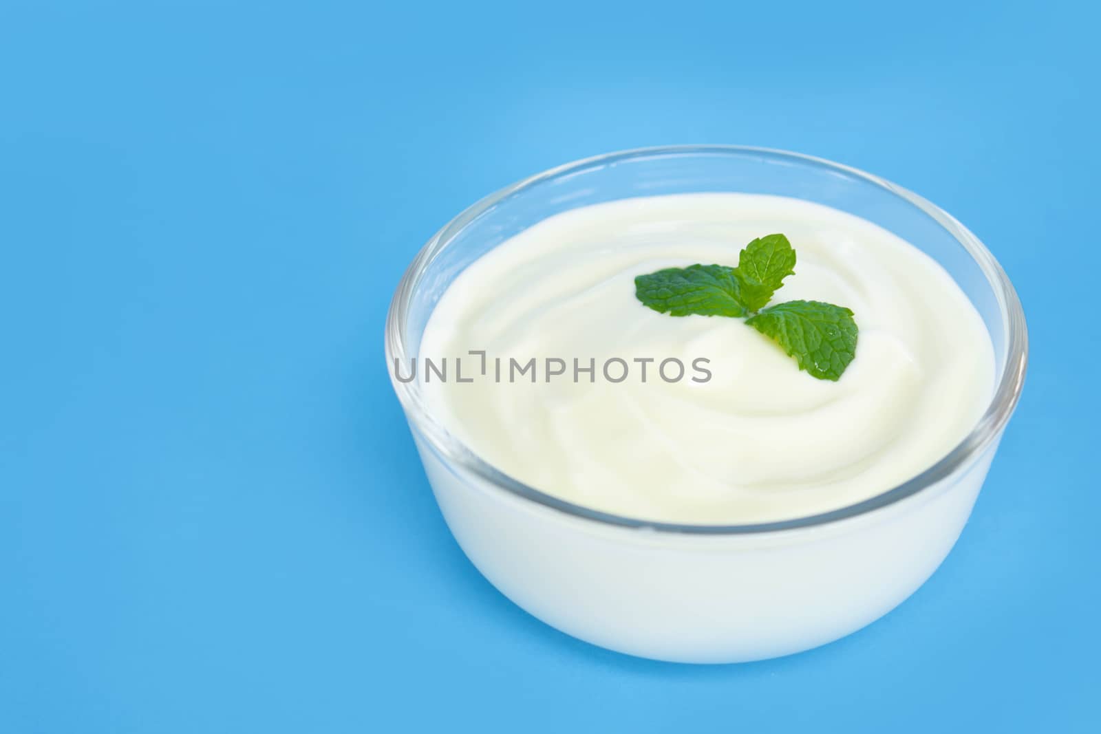 Close up yogurt  in glass bowl  with wooden spoon on blue background