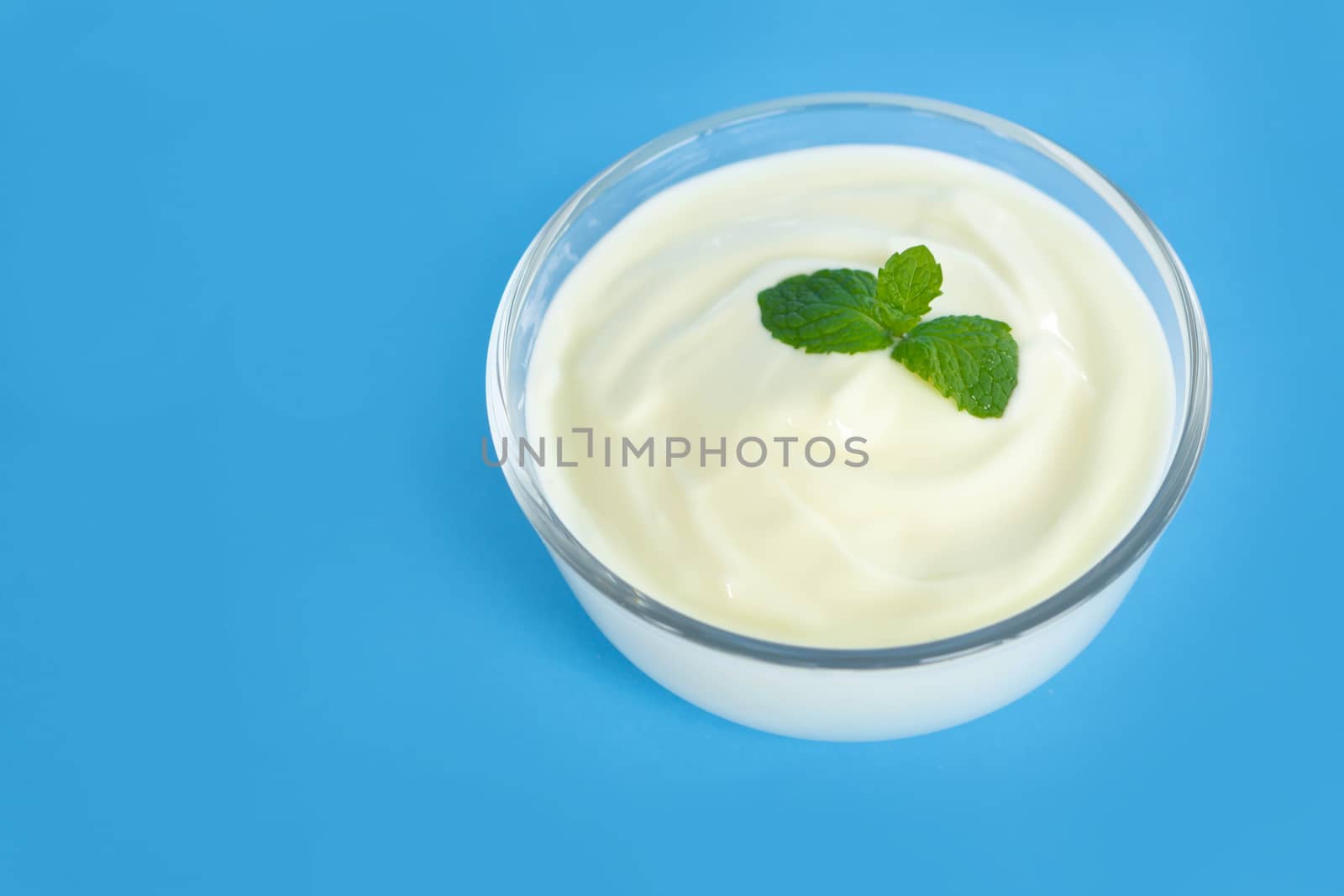 Close up yogurt  in glass bowl  with wooden spoon on blue background