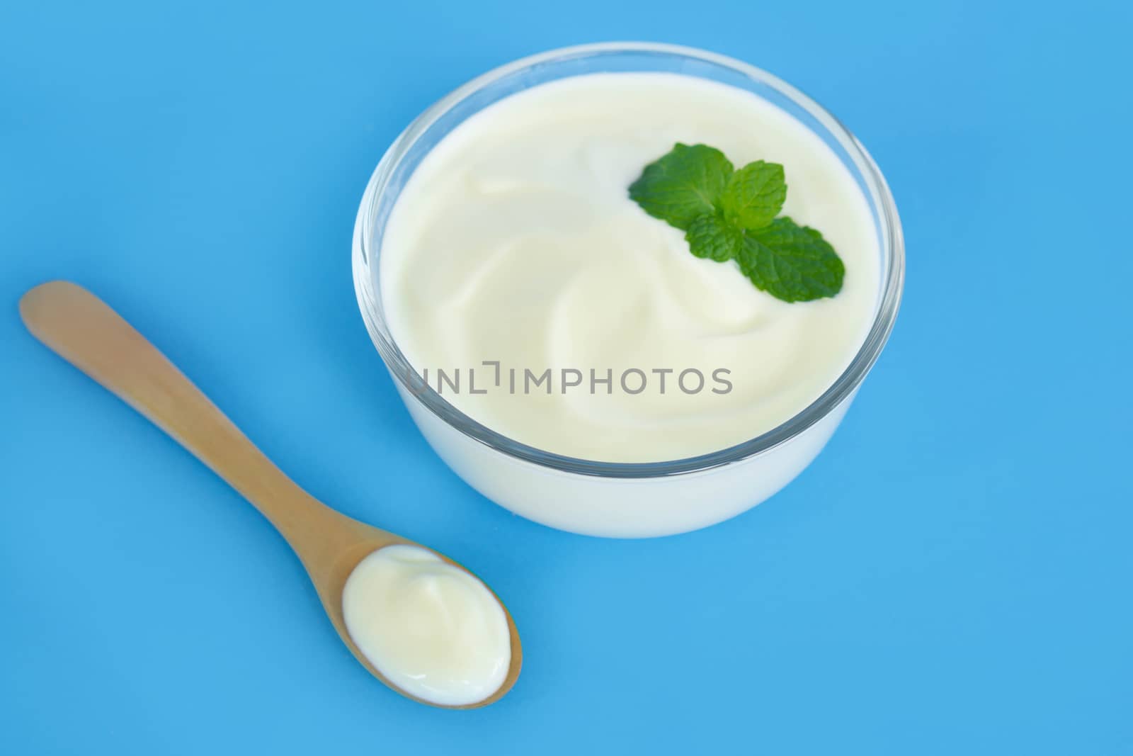 Close up yogurt  in glass bowl  with wooden spoon on blue background