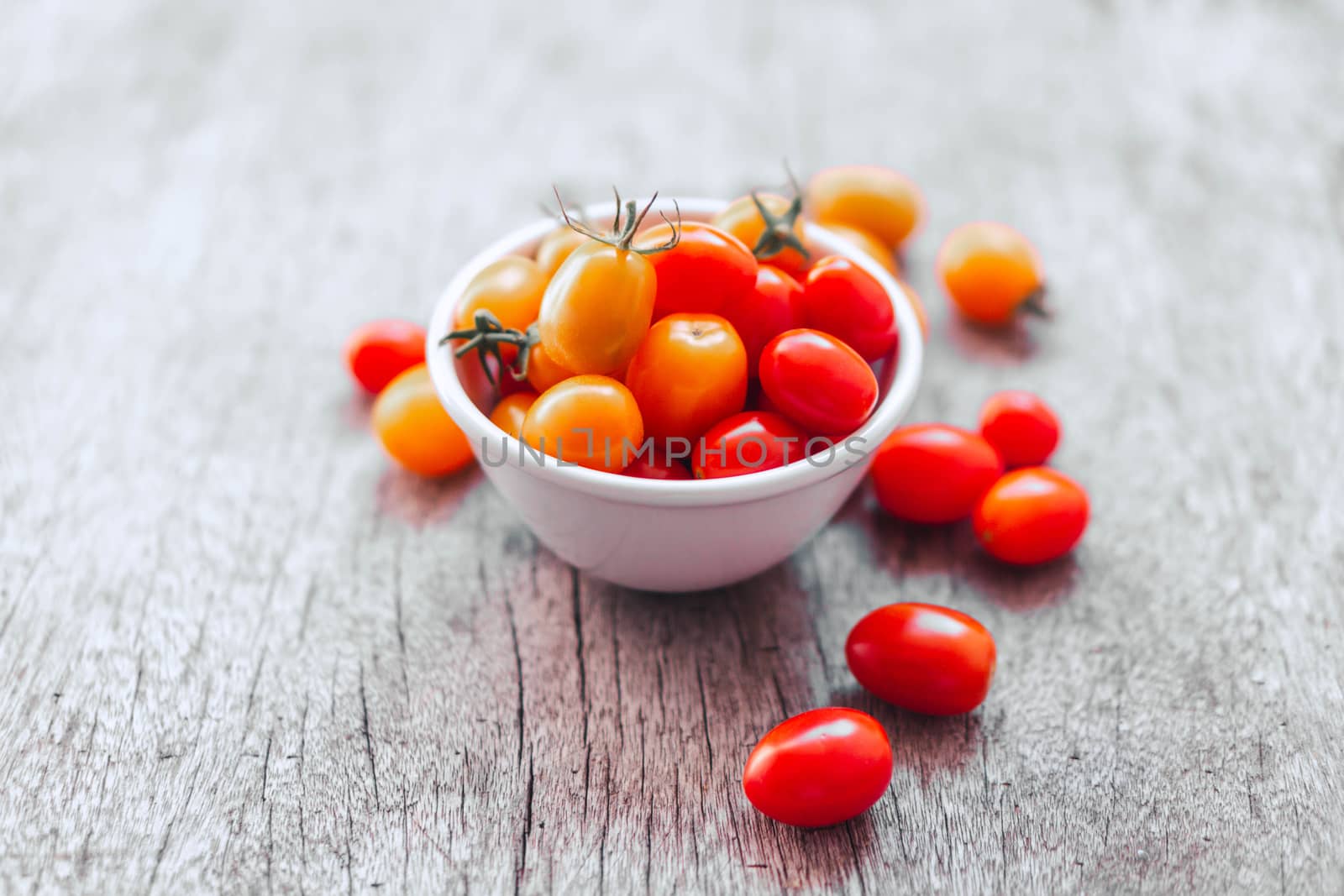 Red cherry tomatoes in white ceramic bowl on old wooden background, vintage tone