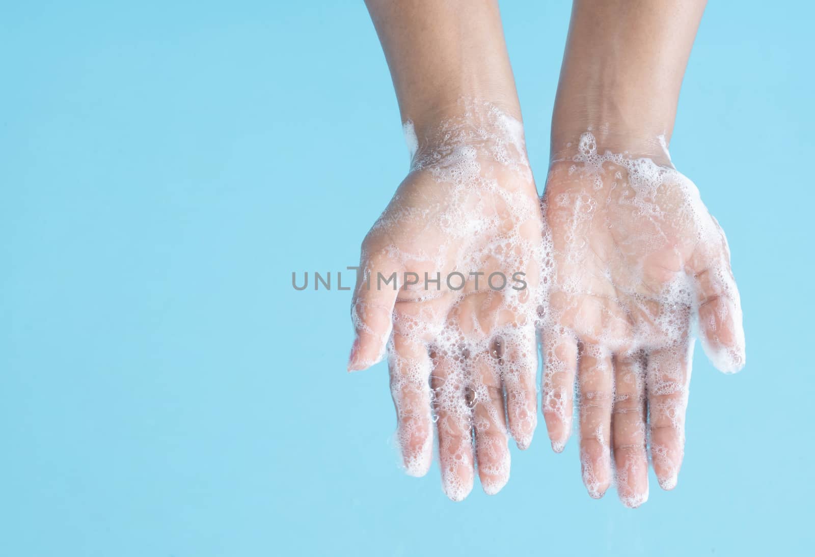 Closeup woman's hand washing with soap on blue background, health care concept