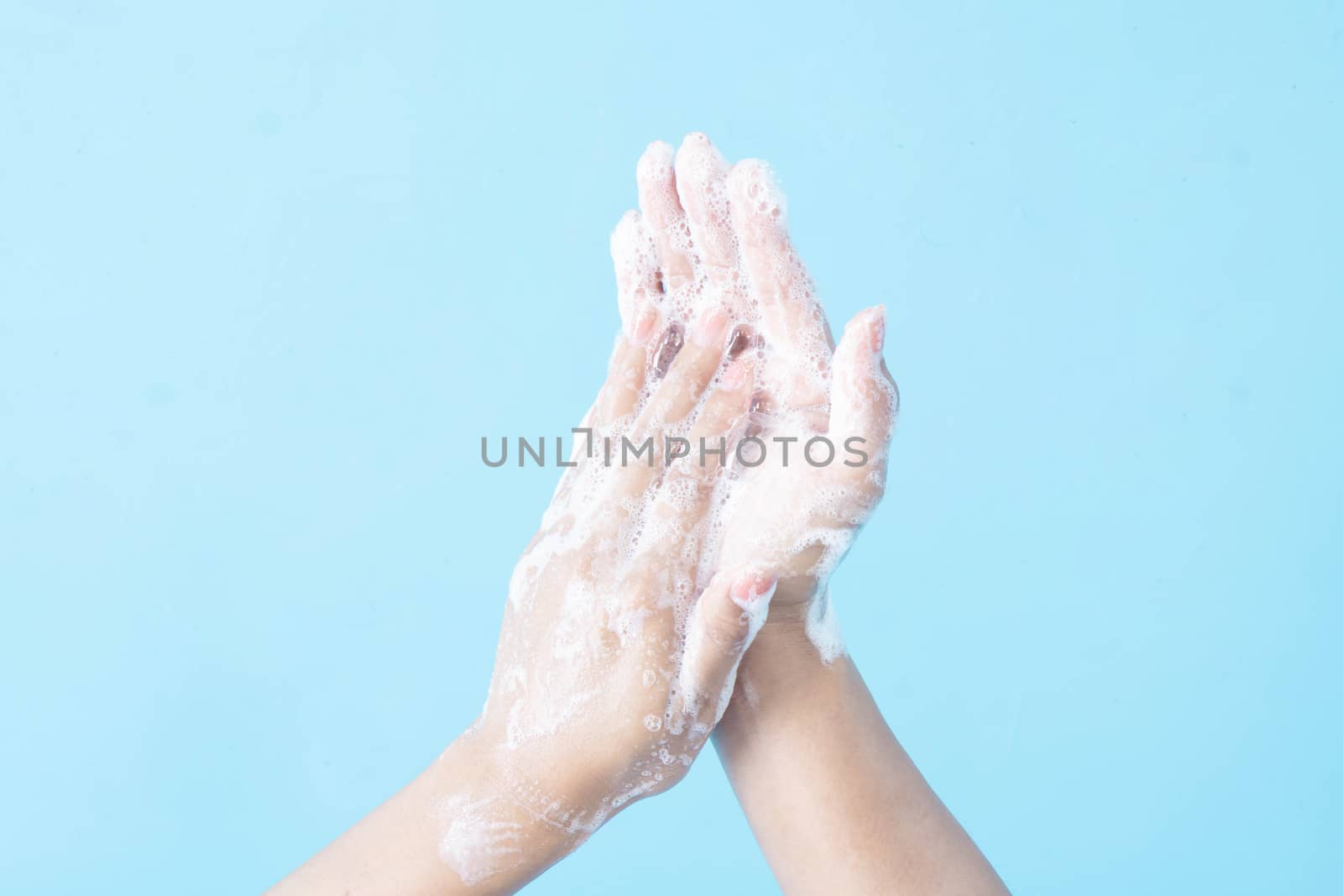 Closeup woman's hand washing with soap on blue background, health care concept