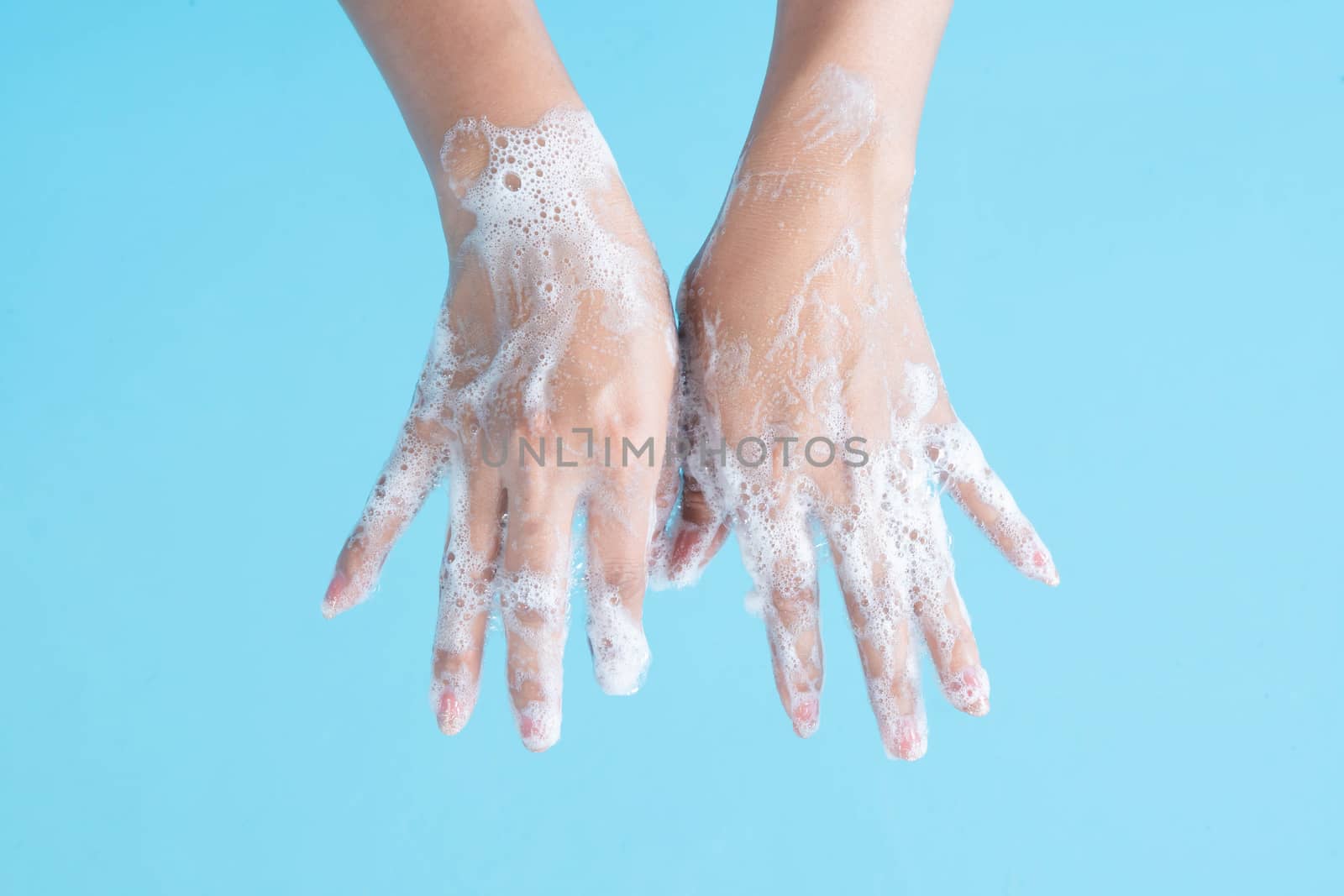 Closeup woman's hand washing with soap on blue background, health care concept