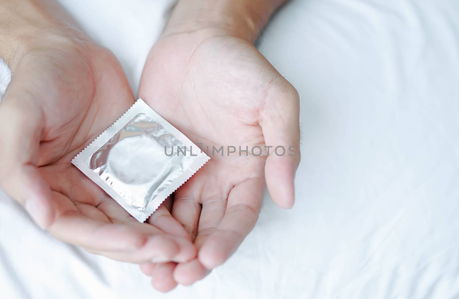 Close up man hand holding condom lying on white bed, health care by pt.pongsak@gmail.com