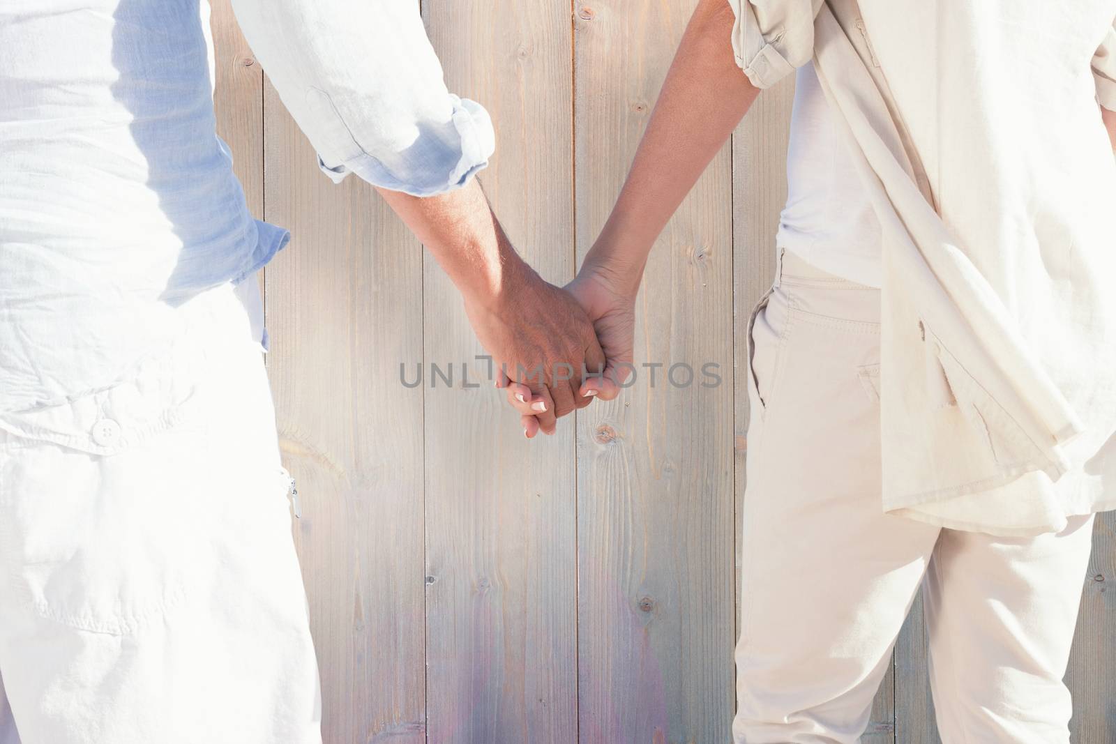 Couple on the beach looking out to sea holding hands against pale grey wooden planks