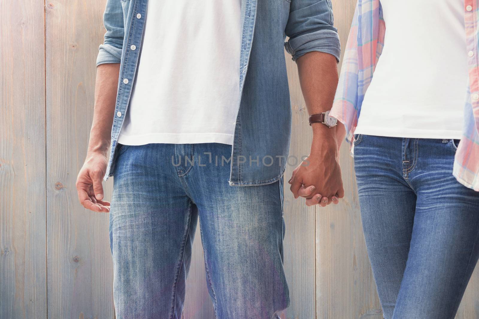 Hip young couple holding hands against pale grey wooden planks