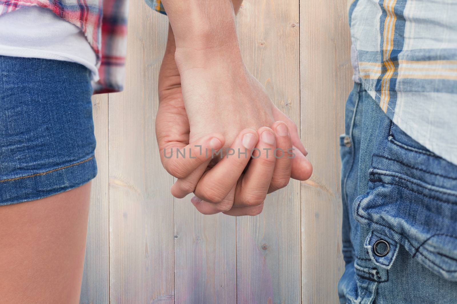 Couple in check shirts and denim holding hands against pale grey wooden planks