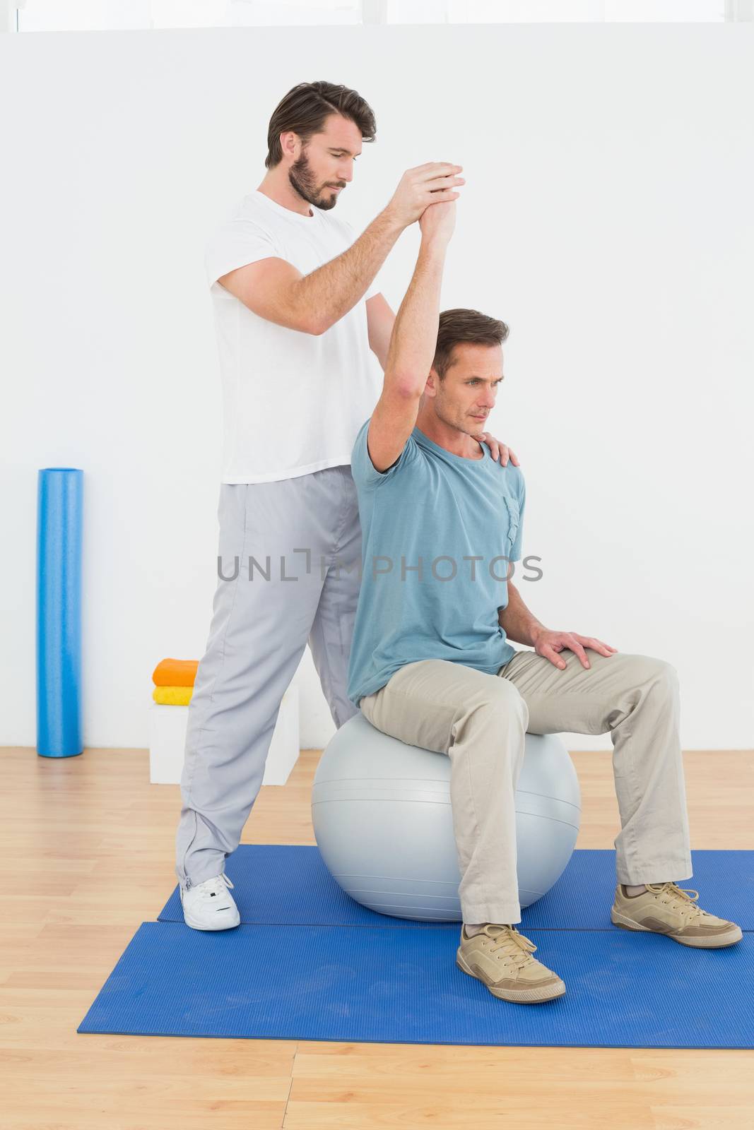 Man on yoga ball working with a physical therapist by Wavebreakmedia