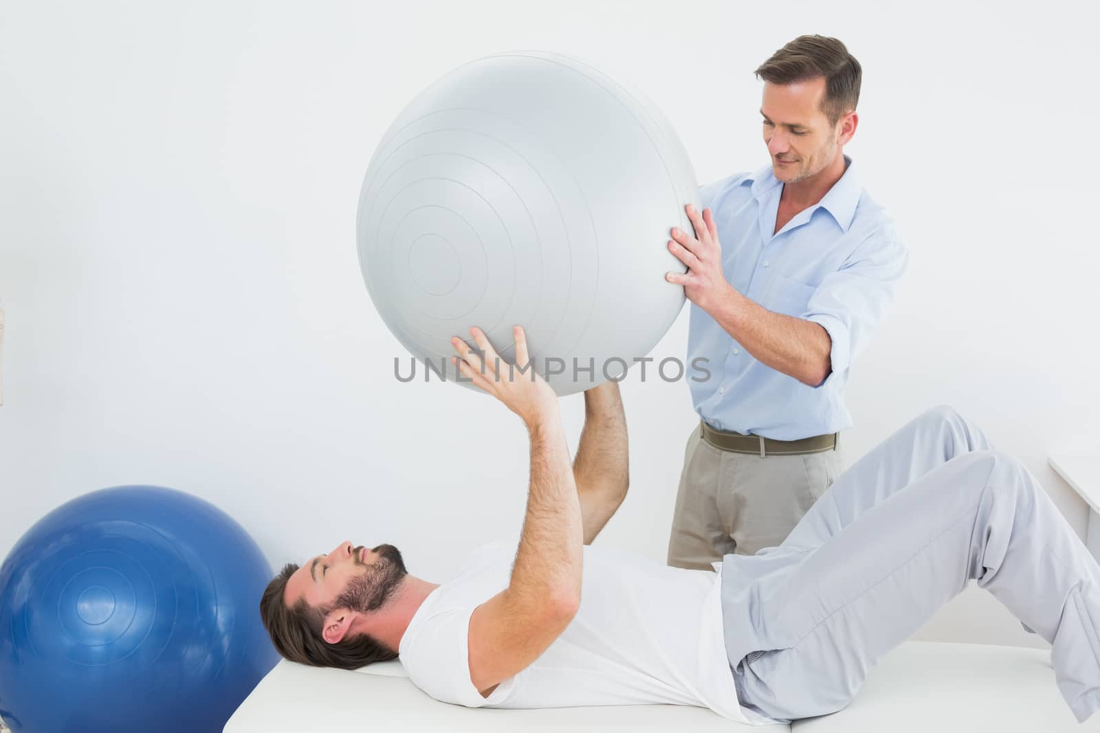 Physical therapist assisting man with yoga ball by Wavebreakmedia