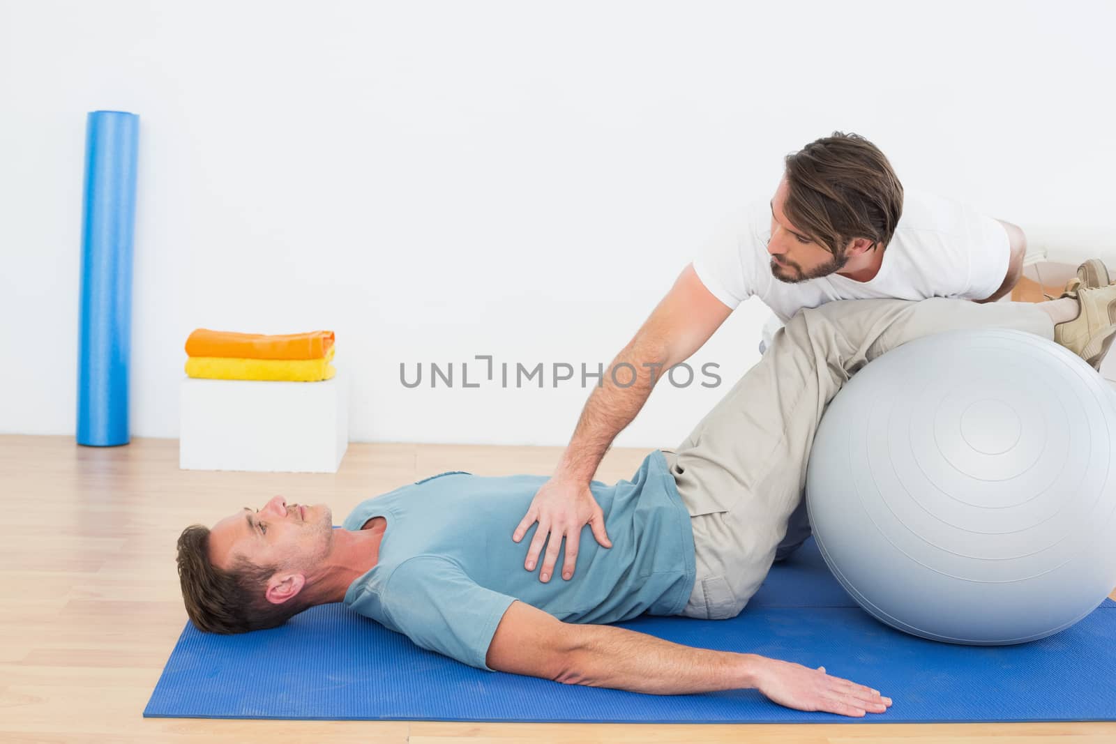 Physical therapist assisting young man with yoga ball in the gym at hospital