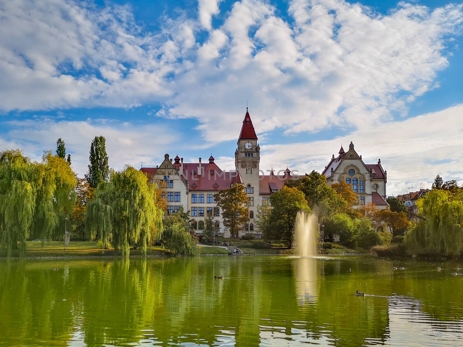 Lake in center of Wroclaw Tolpa Park with fountain in center with faculty of architecture of Wroclaw University by Wierzchu