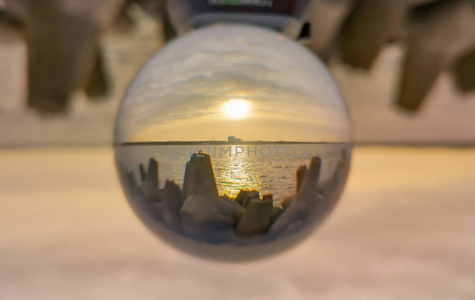 Sunset over baltic sea and coast of Swinoujscie city seen from breakwater in crystal glassball reflection