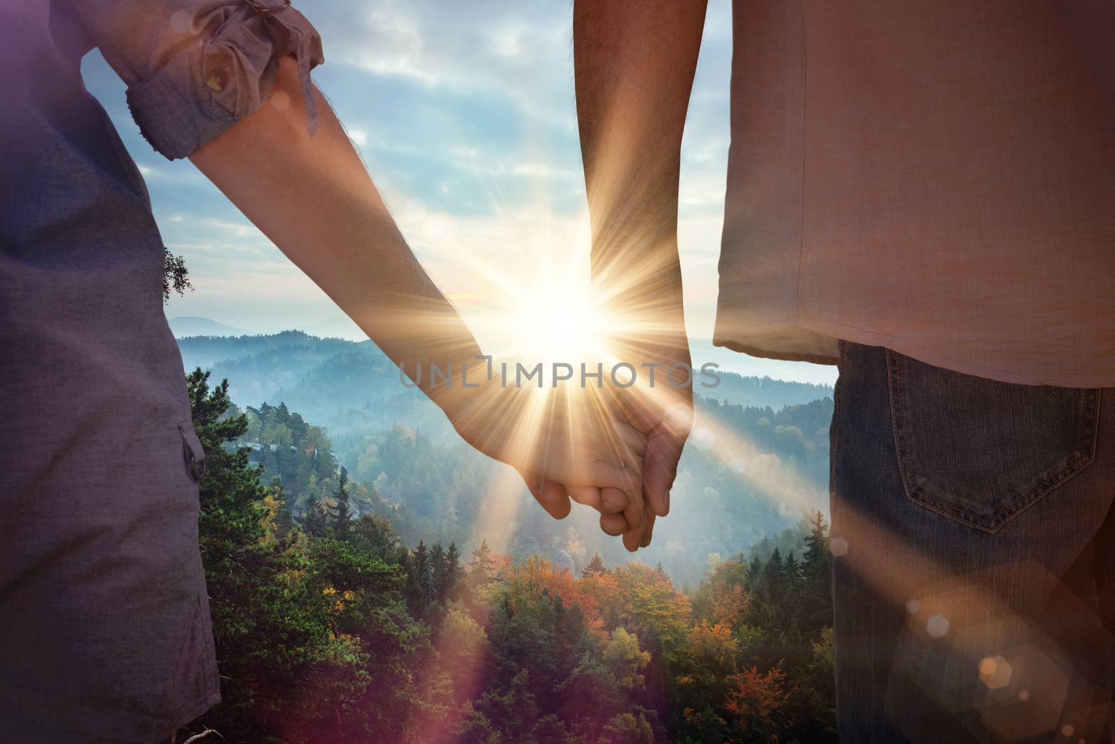 Couple holding hands in park against sunrise over mountains