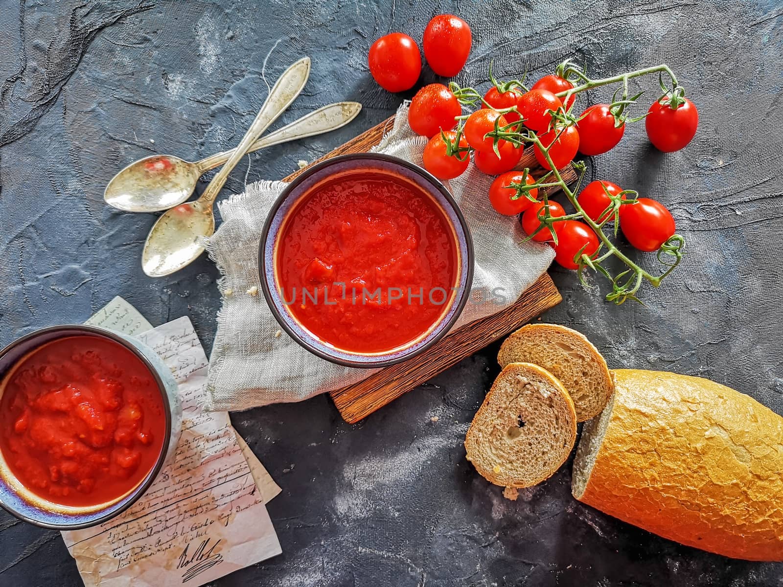Flat lay of tomato soup with paper notes, bread, old spoons and cherry tomatoes