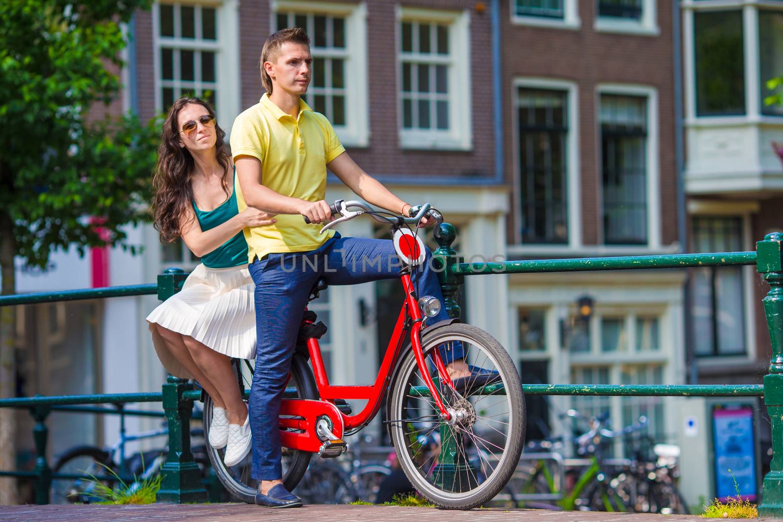 Young happy caucasian couple on bikes in old streets in Amsterdam by travnikovstudio