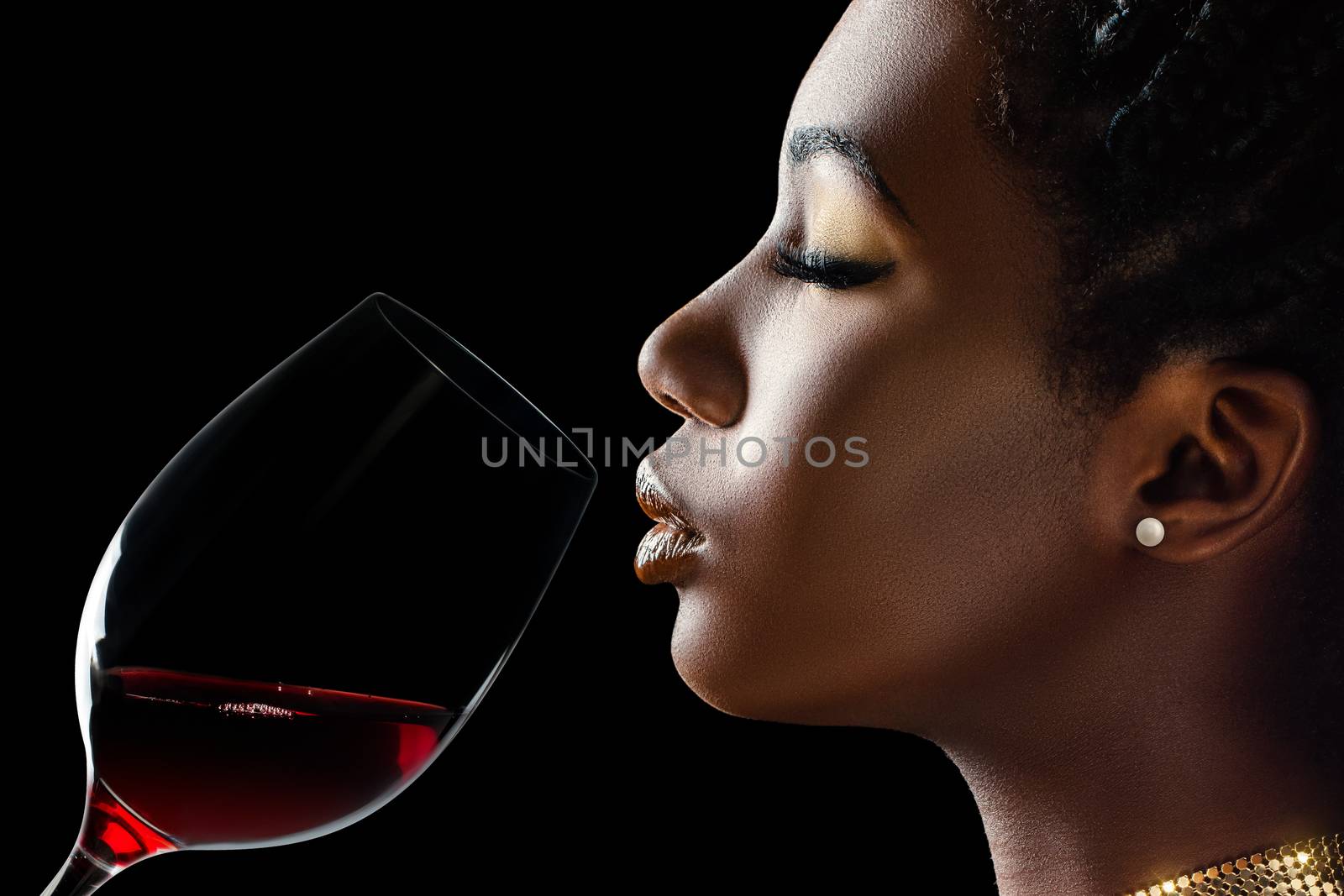 Macro close up low key portrait of sensual african woman smelling red wine.Side view of girl with red wine glass next to face against black background.