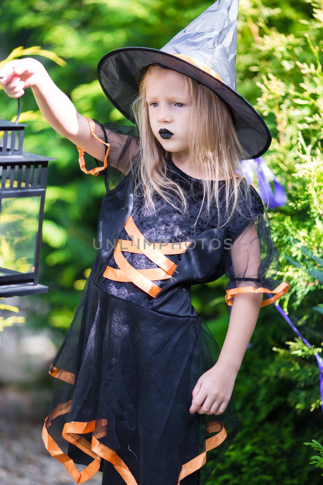 Adorable amasing little girl wearing witch costume on Halloween outdoors. Trick or treat. by travnikovstudio