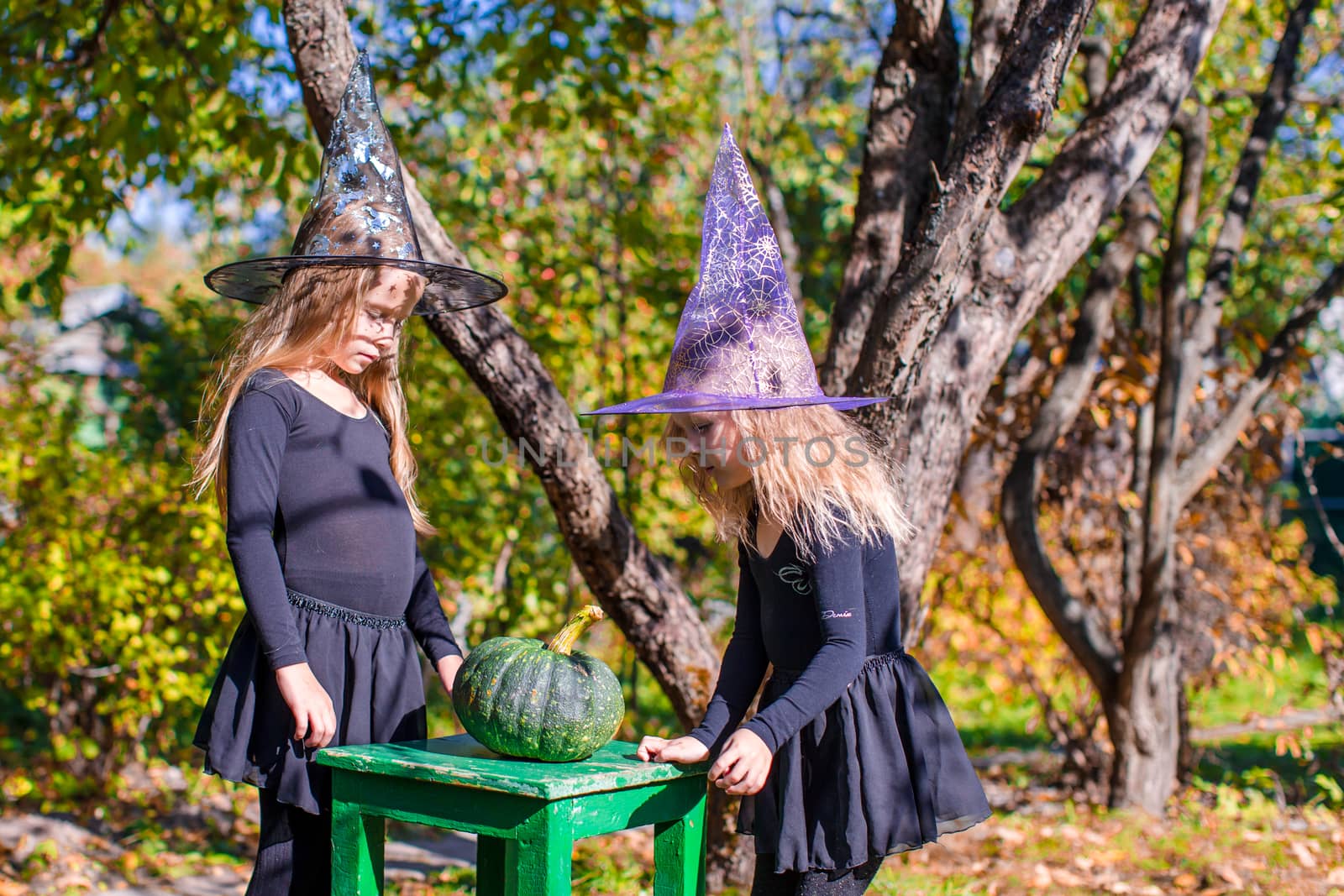 Adorable little witches have fun outdoors on Halloween. Trick or treat. by travnikovstudio