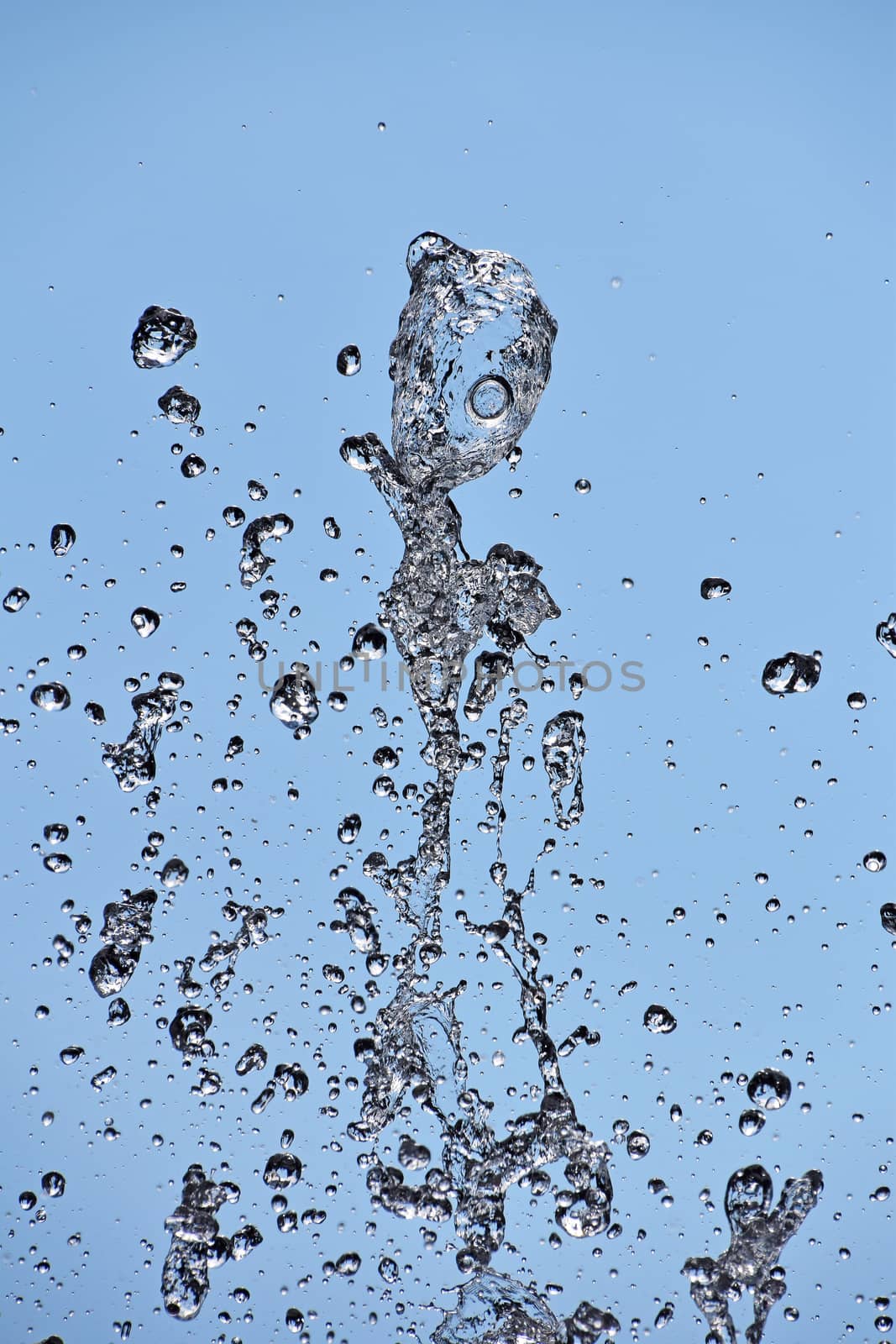 Close up water drops of fountain stream splash over background of clear blue sky