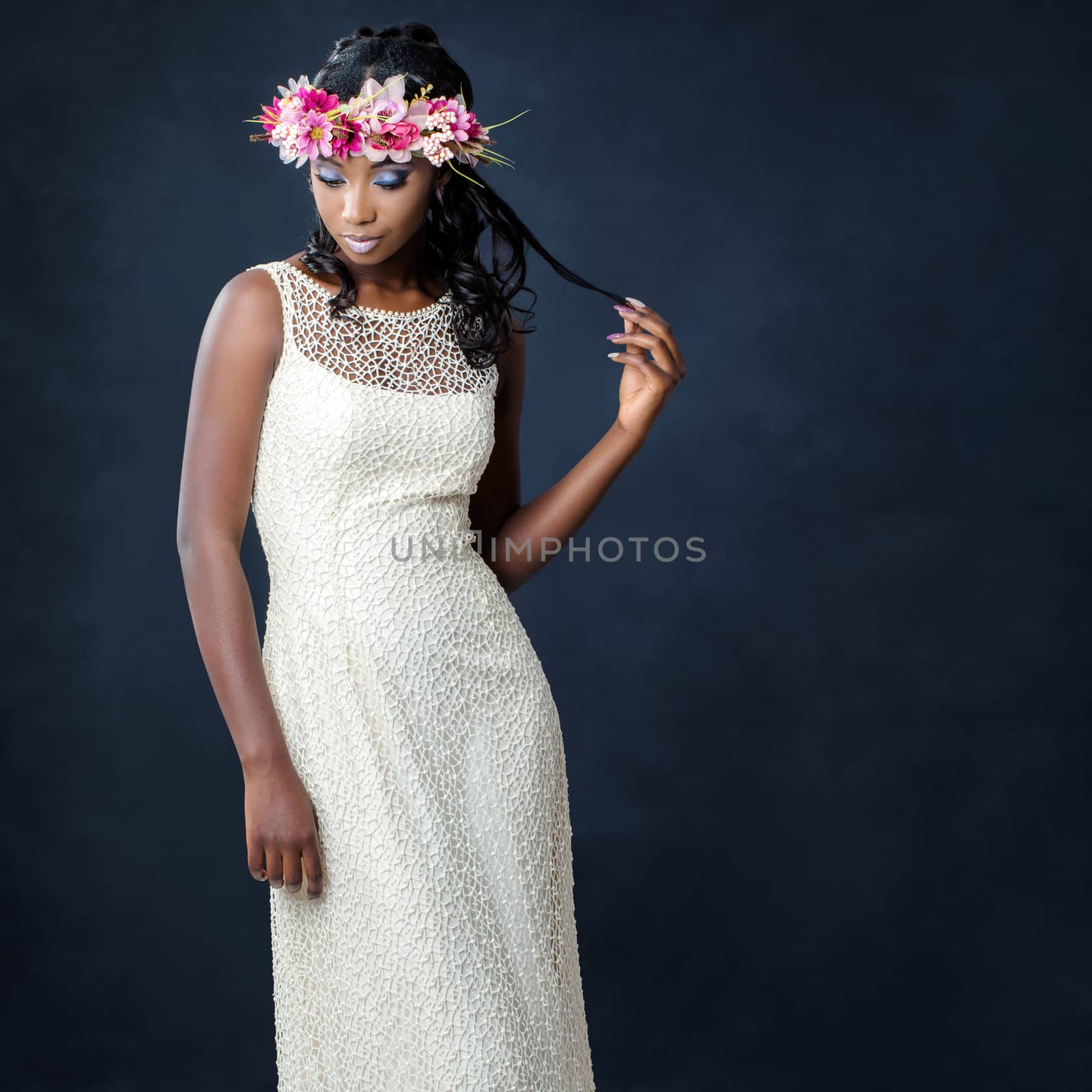Close up studio portrait of elegant young african bride wearing colorful flower garland.Woman on white designer wedding dress against dark background.