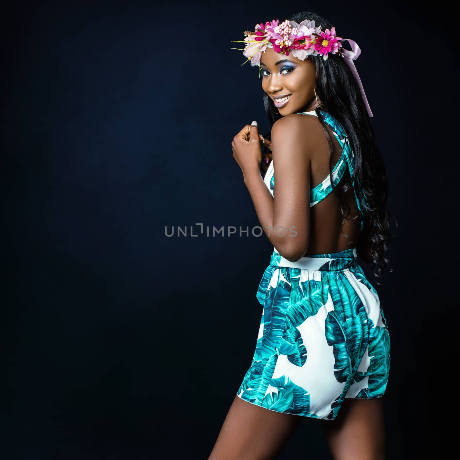 Close up studio portrait of beautiful young african girl wearing colorful flower garland against dark background.