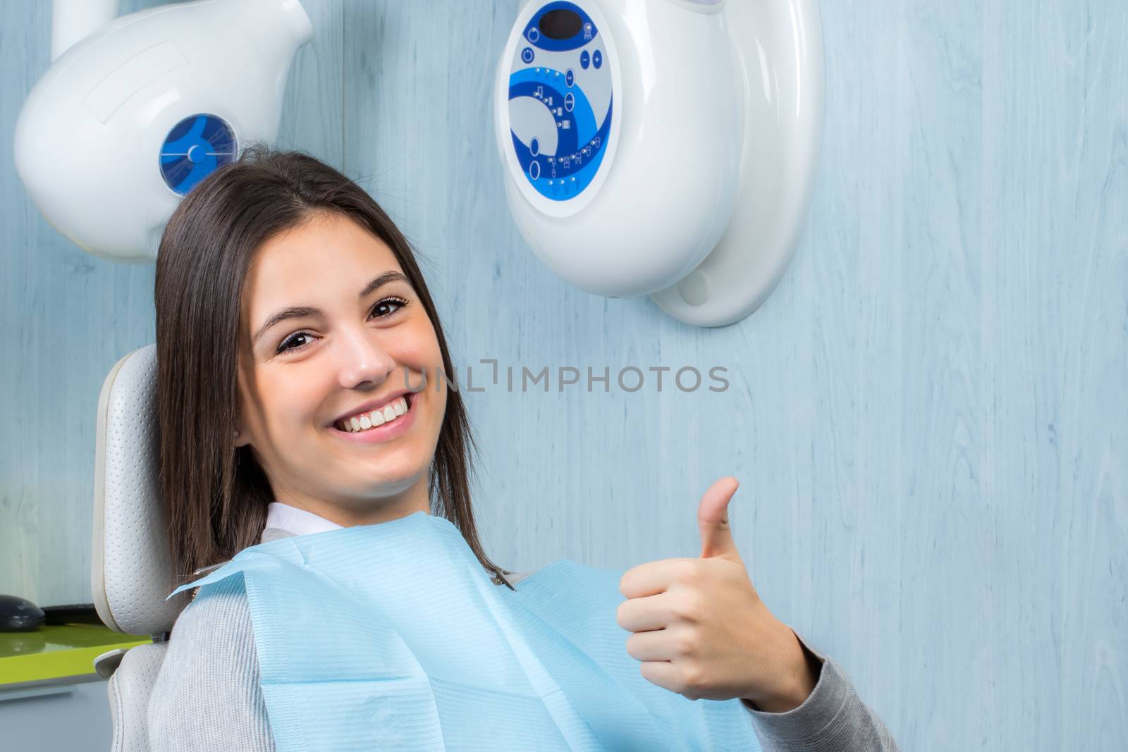 Close up portrait of cute young woman doing thumbs up at appointment in dental clinic.