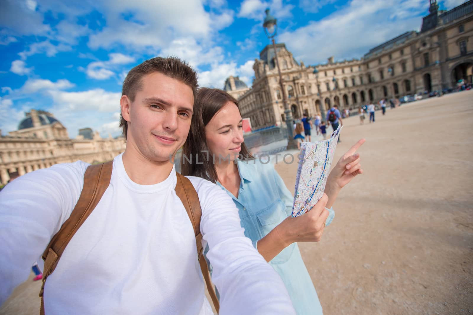 Happy young family with map of european city taking selfie in Paris by travnikovstudio