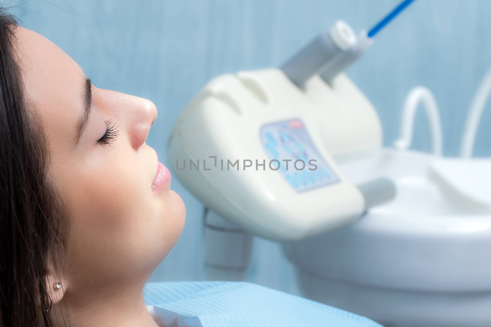 Close up side view portrait of young woman at dental check up.Girl laying with eyes closed with equipment in background.