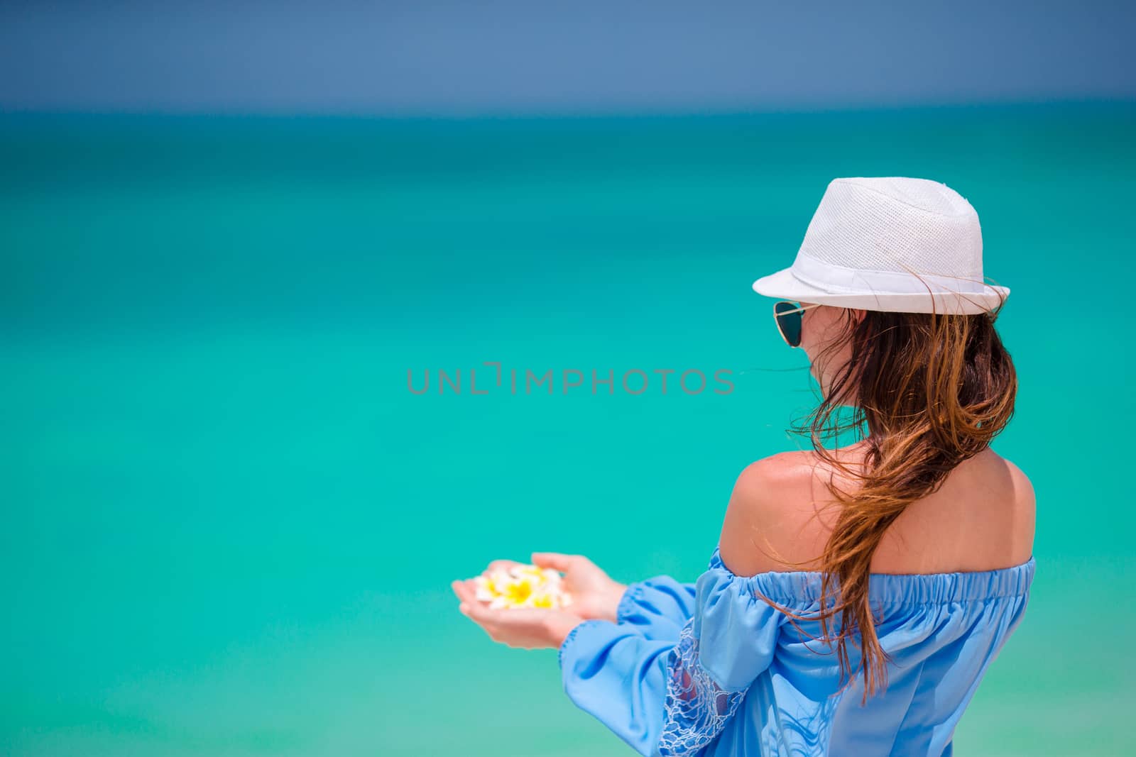 Beautiful frangipani flowers in female hands background turquoise sea on white beach by travnikovstudio