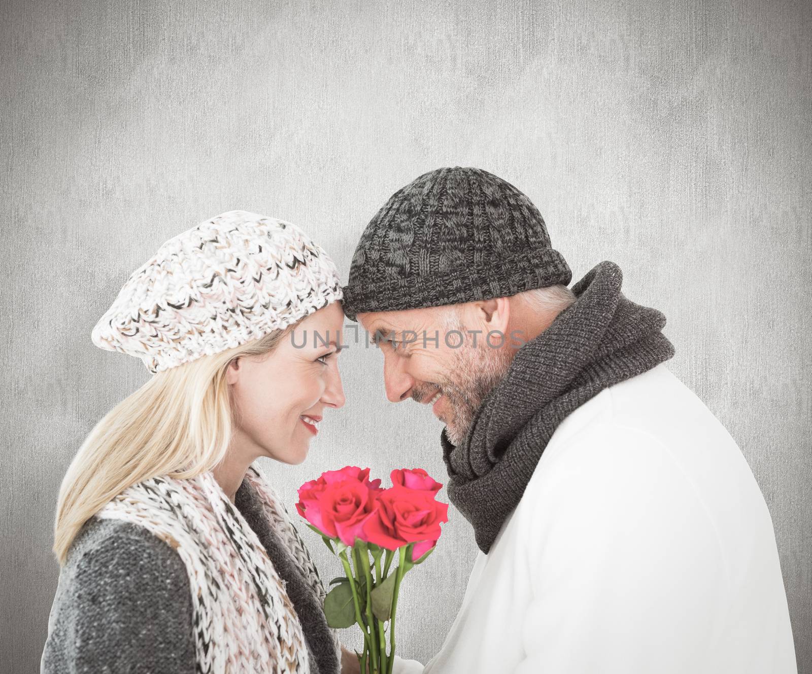 Smiling couple in winter fashion posing with roses against weathered surface 
