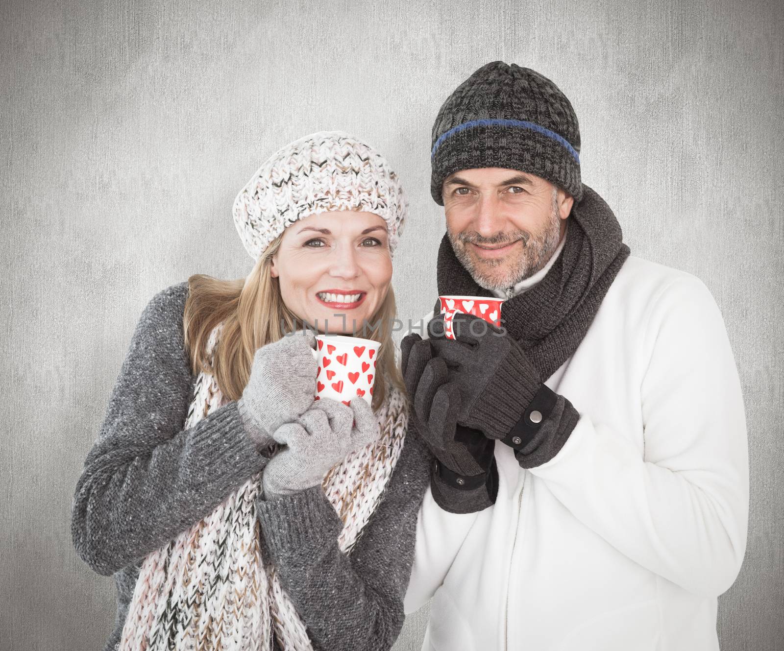 Happy couple in winter fashion holding mugs against weathered surface 