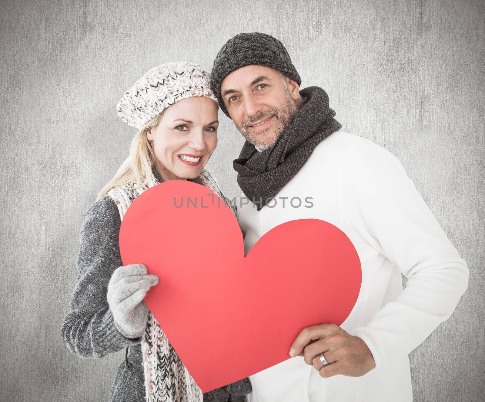 Smiling couple in winter fashion posing with heart shape against weathered surface 
