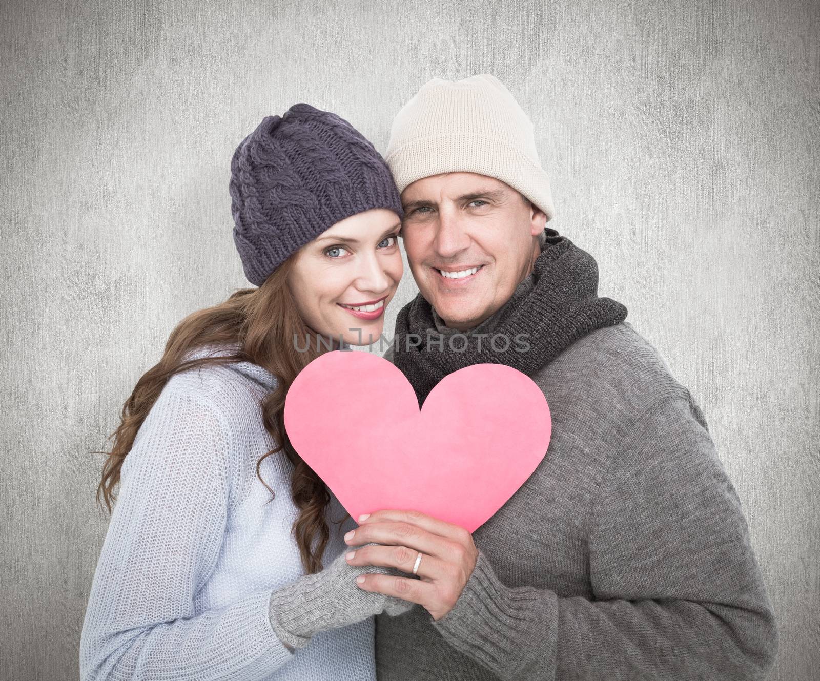 Composite image of happy couple in warm clothing holding heart by Wavebreakmedia
