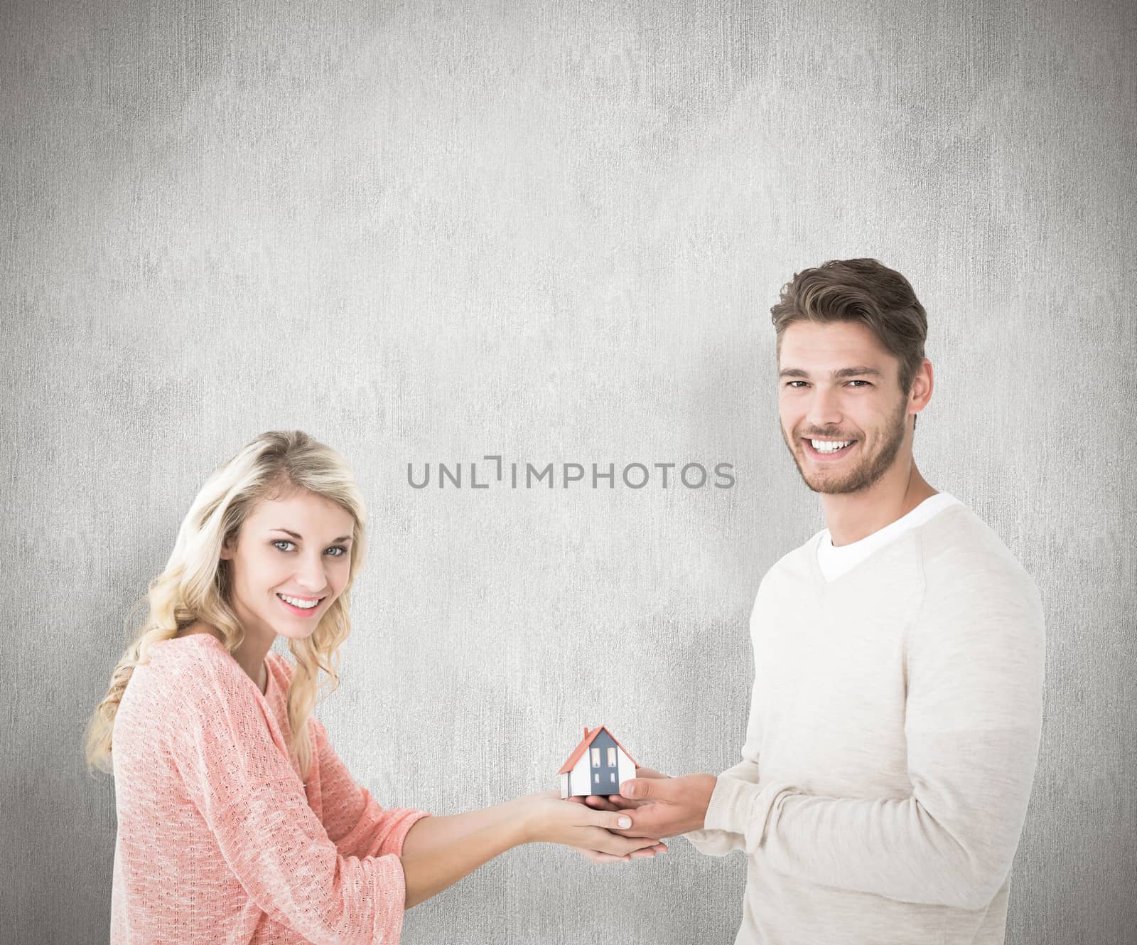 Attractive couple holding miniature house model against white background
