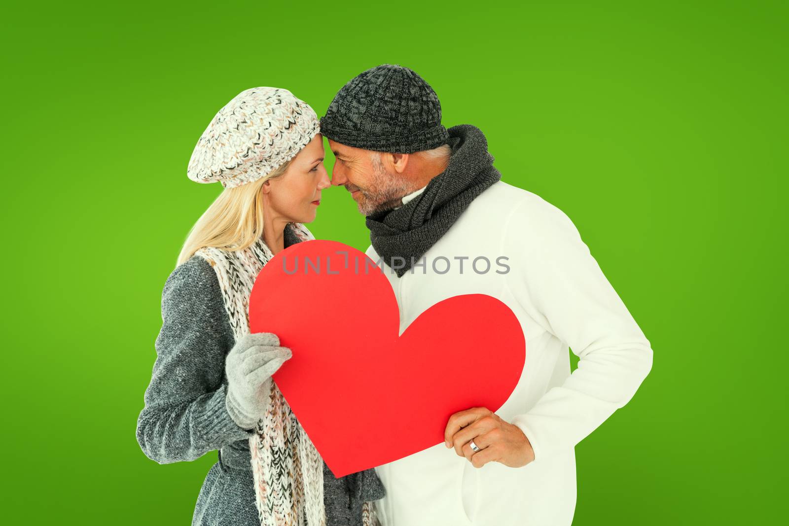 Smiling couple in winter fashion posing with heart shape against green vignette