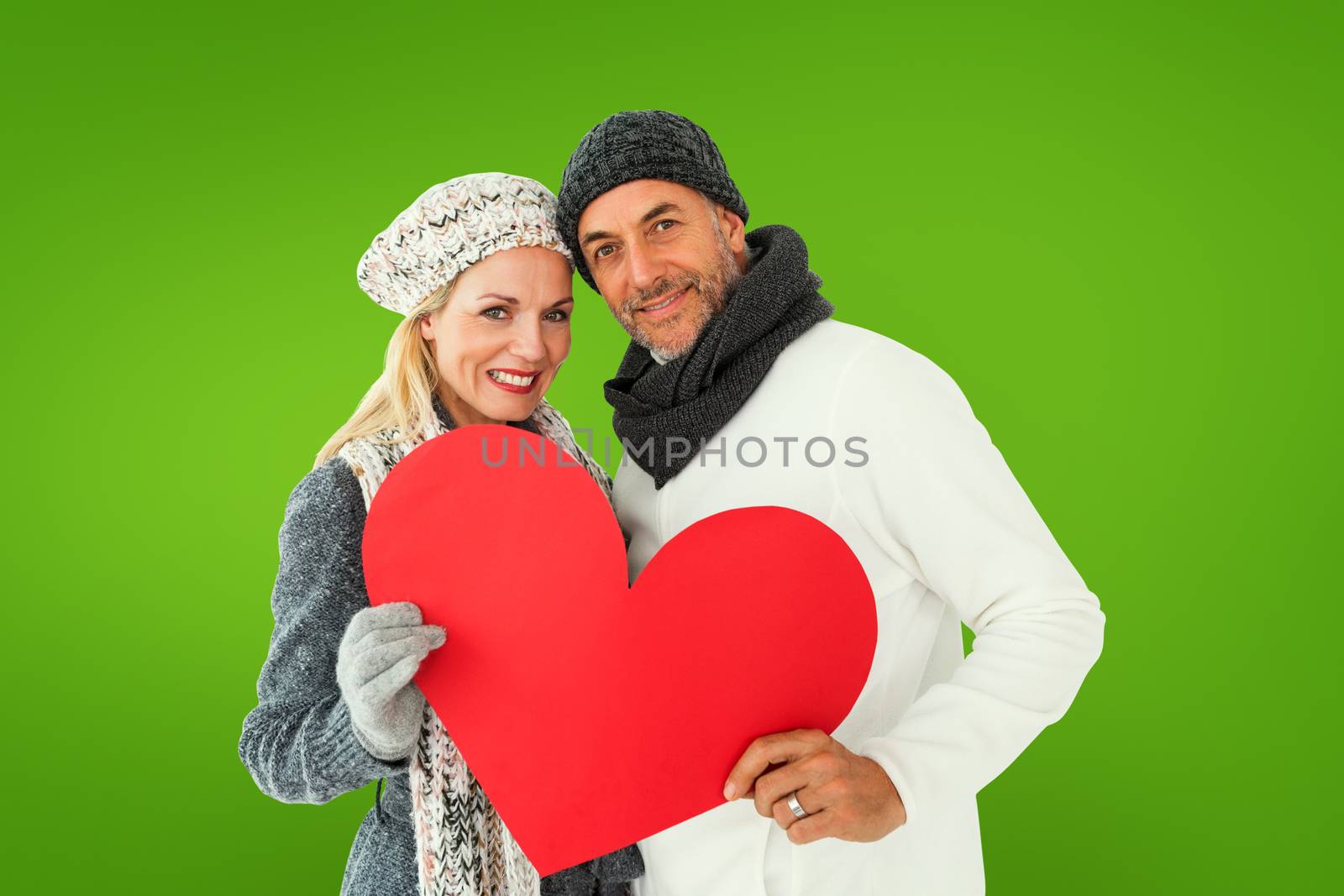 Smiling couple in winter fashion posing with heart shape against green vignette