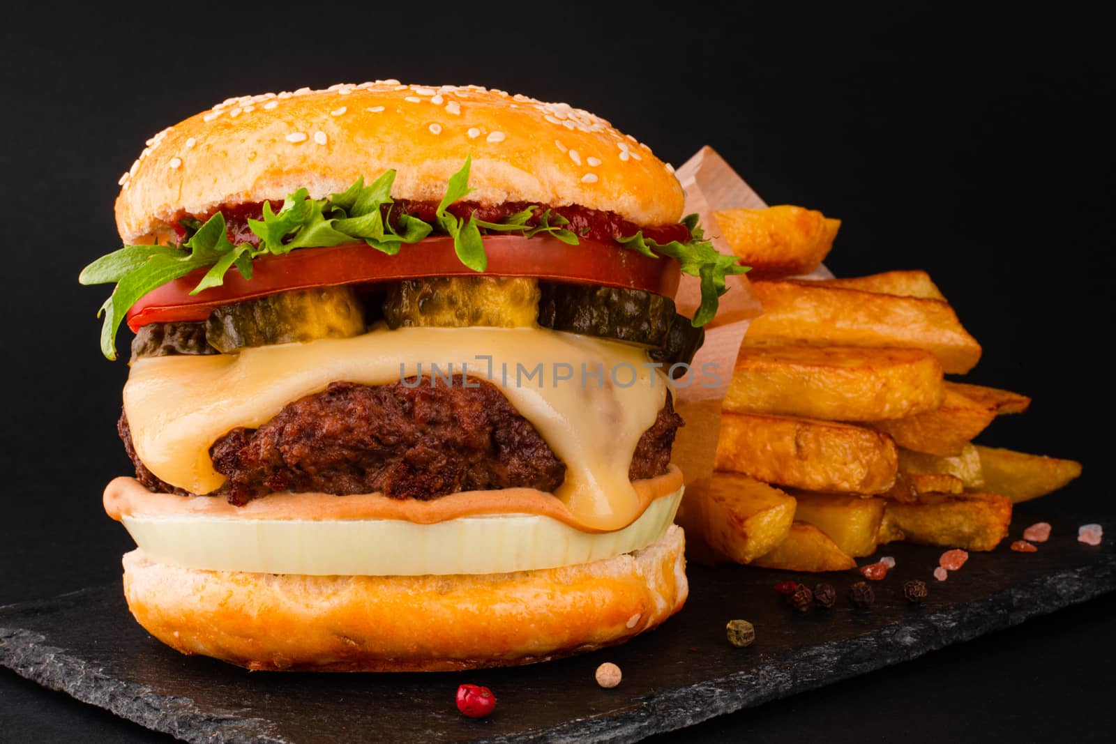 One big tall classic hamburger burger cheeseburger with french fries on black stone plate on black background with copy space for text