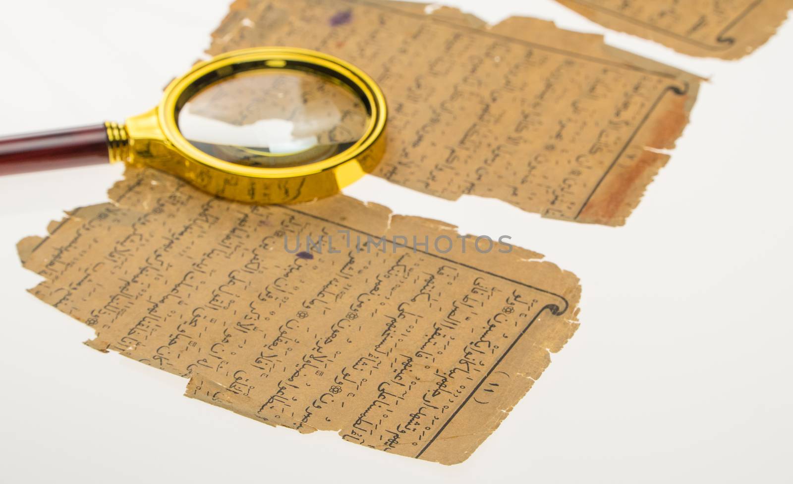 Book pages with an Arabic manuscript on a table with a light and a magnifying glass. Paleography, the study of ancient Arabic writing