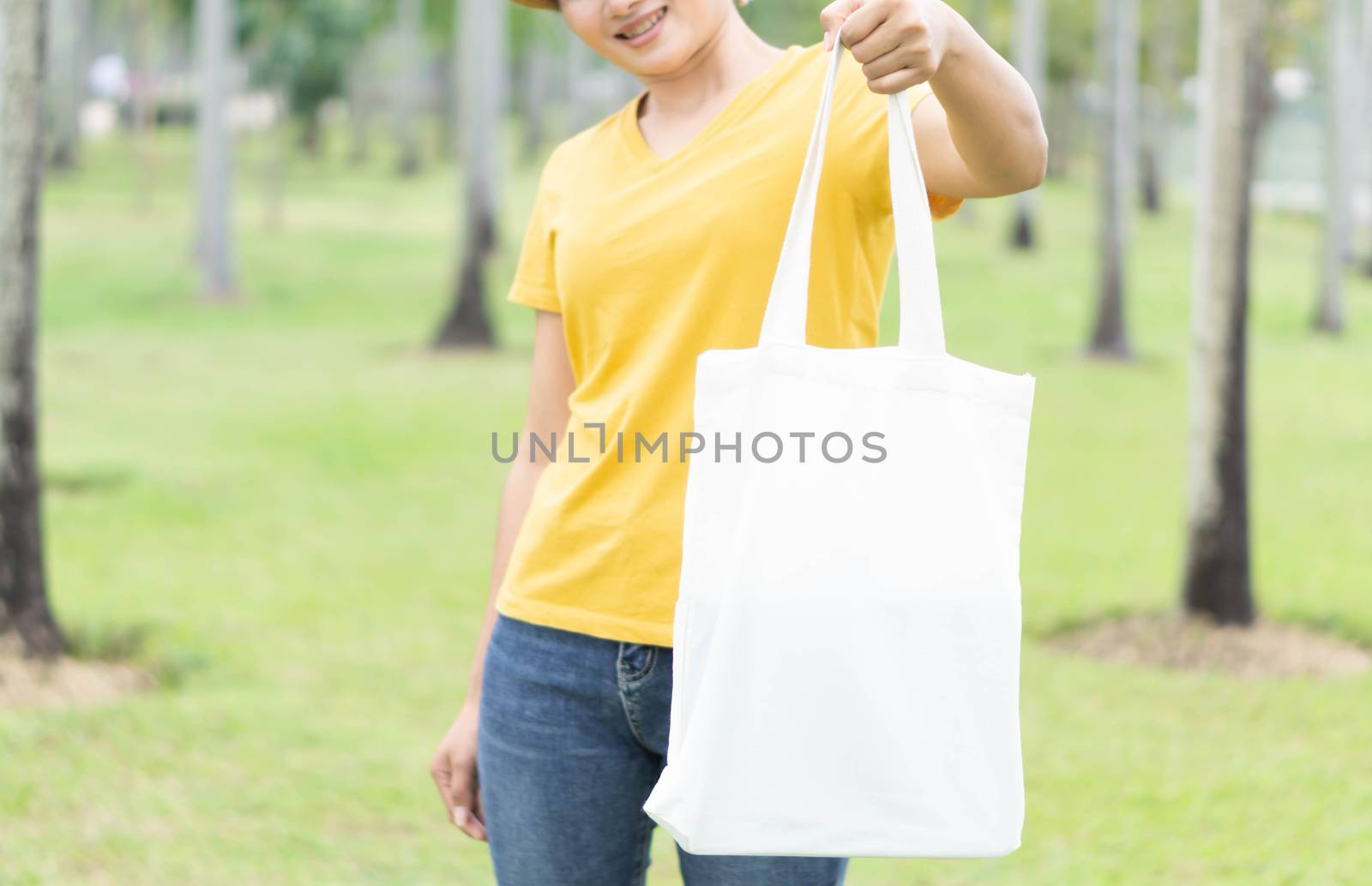 Closeup woman hand holding white bag canvas fabric with green nature background, Save the world concept