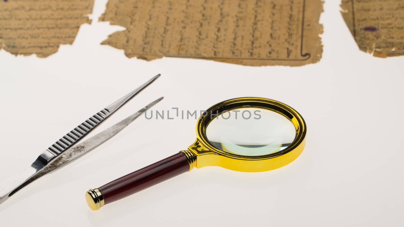 Book pages with an Arabic manuscript on a table with a light and a magnifying glass. Paleography, the study of ancient Arabic writing