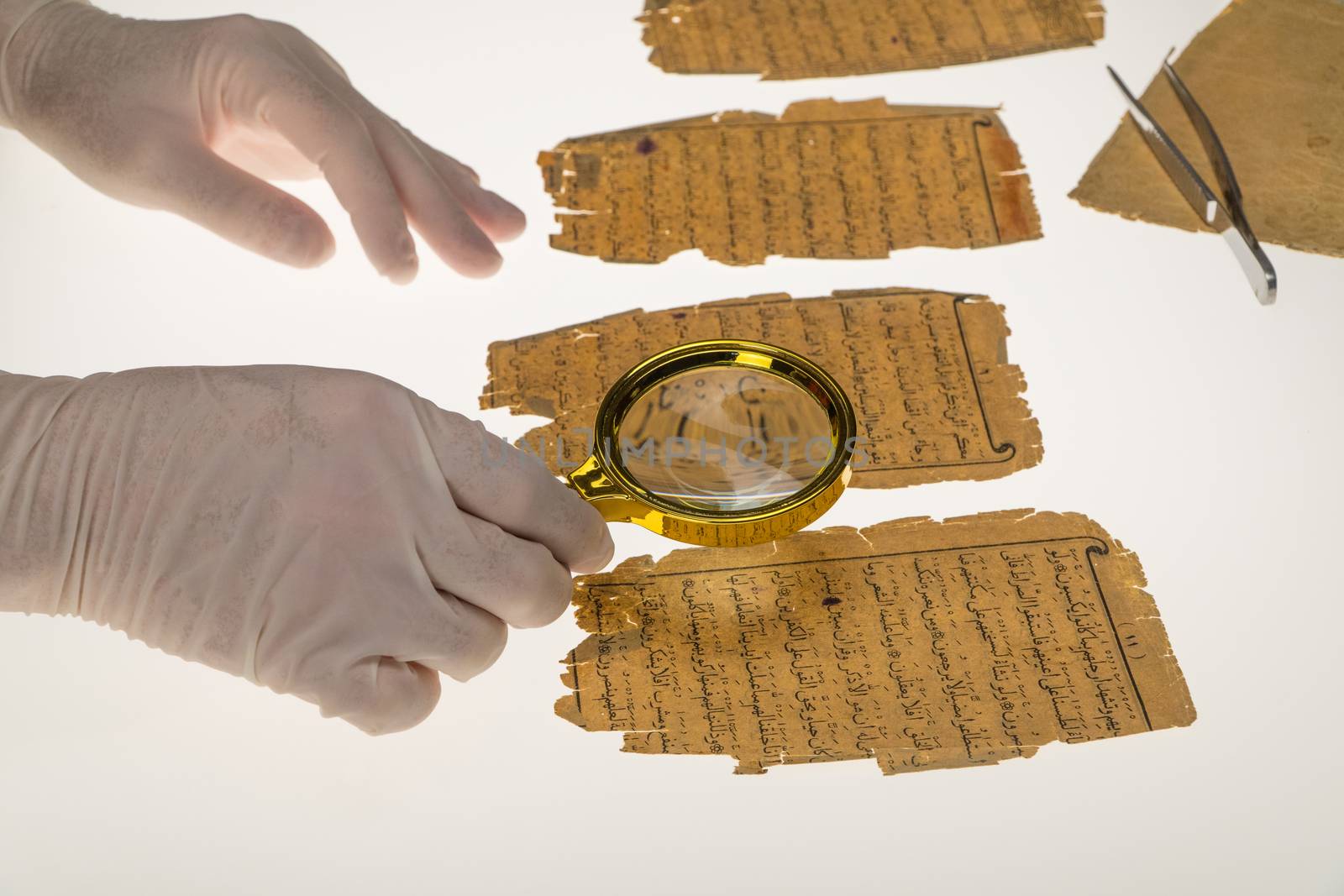 A researcher studies Arabic writing from the Koran using a magnifying glass and a table with a light. Paleography, the study of ancient Arabic writing