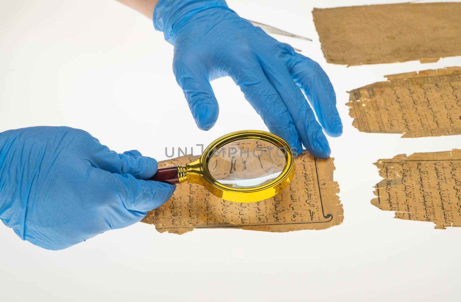 A researcher studies Arabic writing from the Koran using a magnifying glass and a table with a light. Paleography, the study of ancient Arabic writing