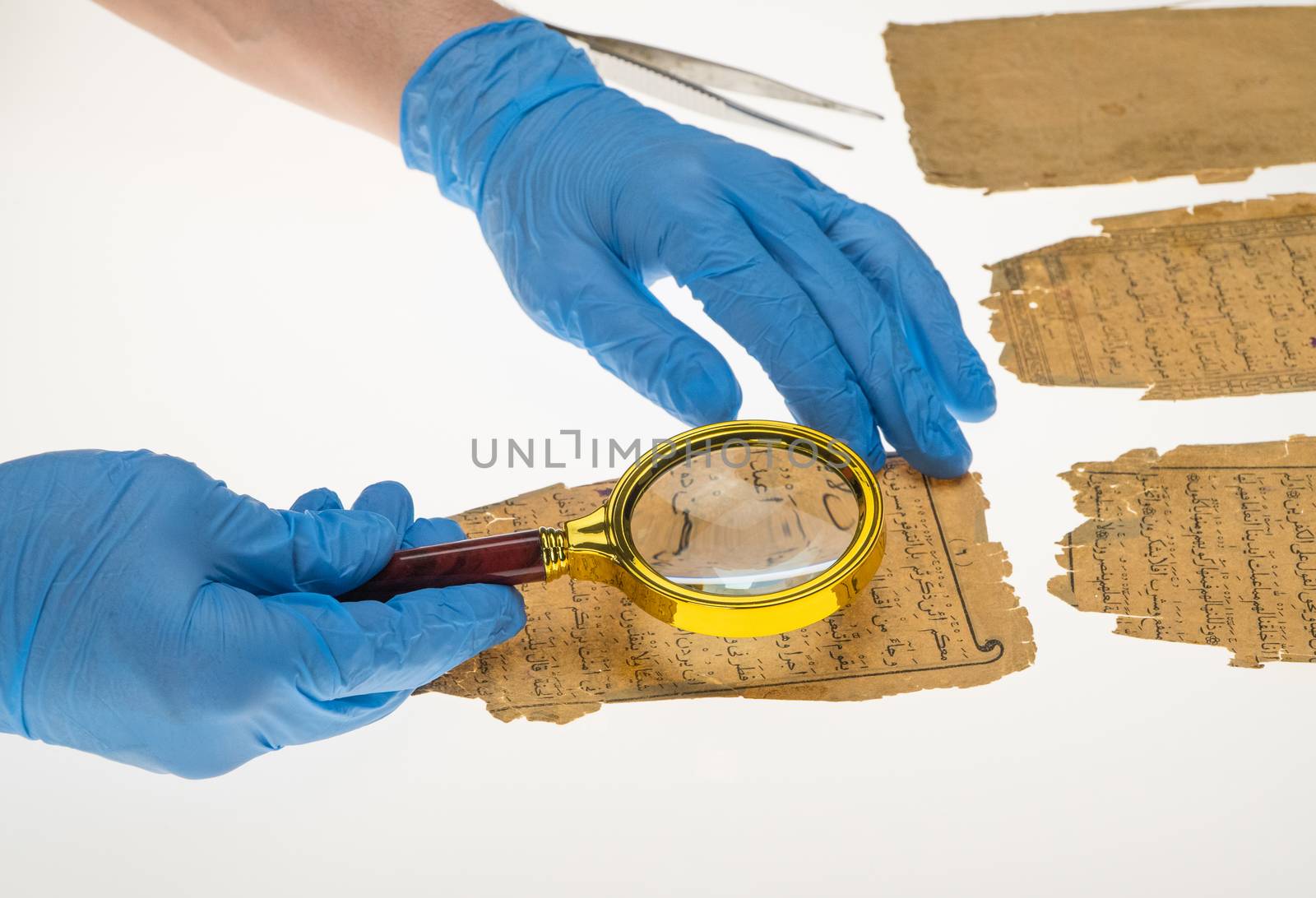 A researcher studies Arabic writing from the Koran using a magnifying glass and a table with a light. Paleography, the study of ancient Arabic writing