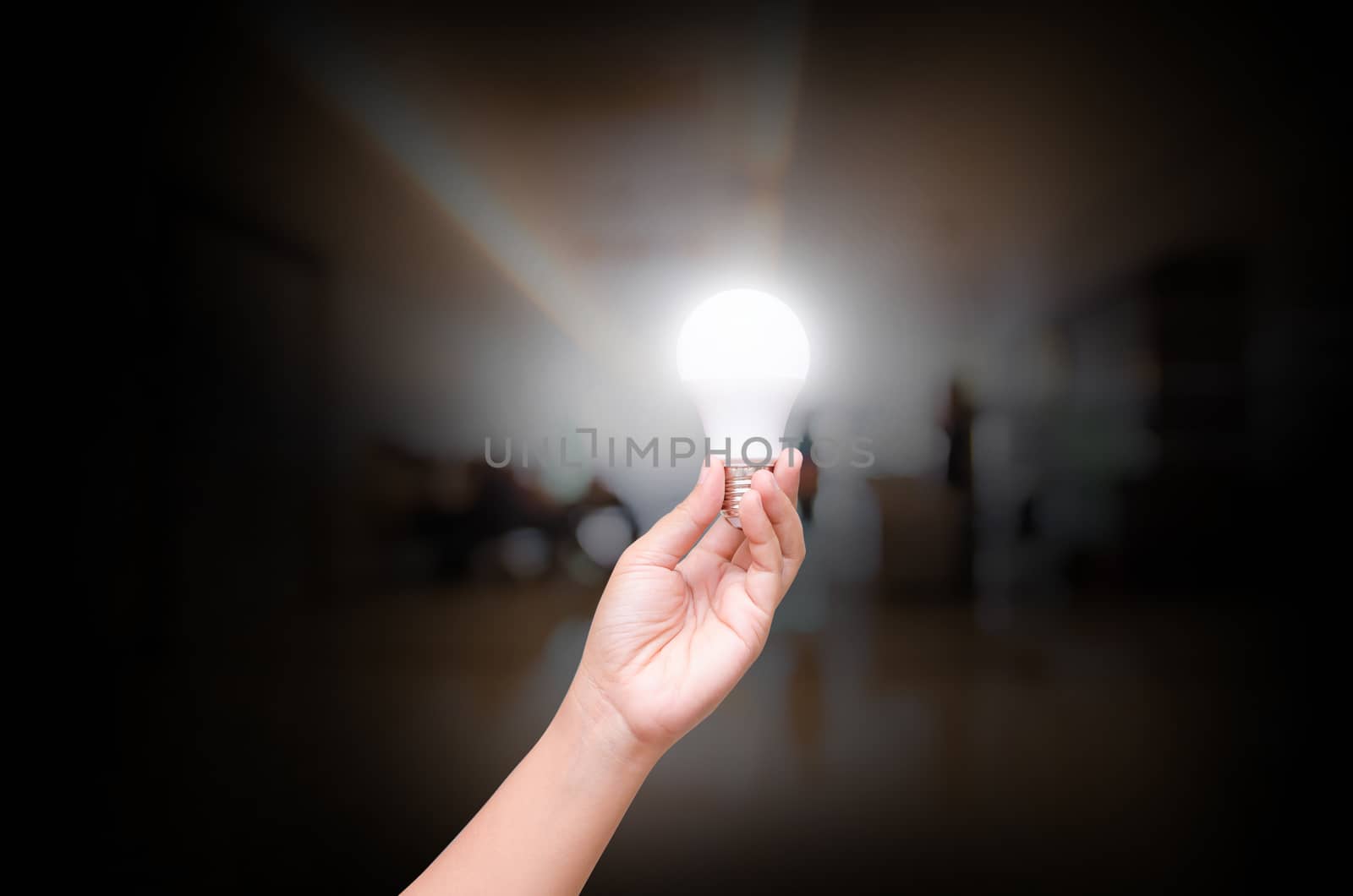 Woman hand hold lighting LED bulb on blurry indoor hall of offic by thekaikoro