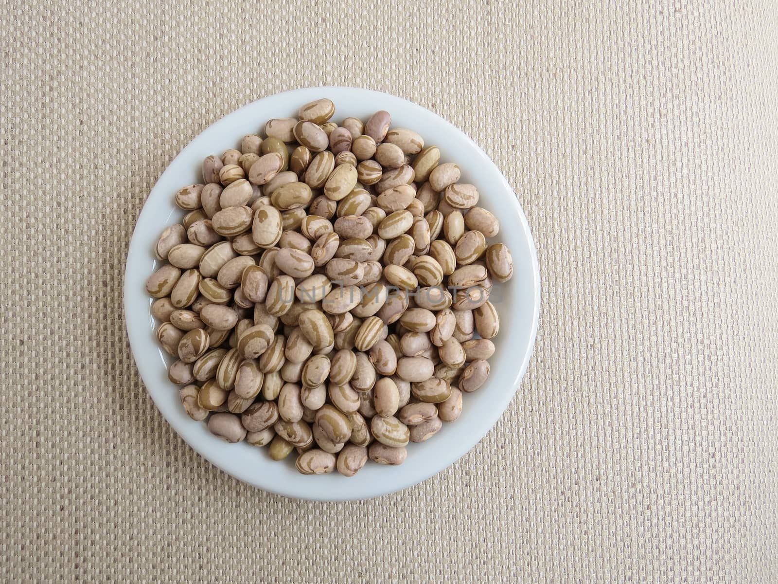 White plate with handful of raw carioca beans on a light cloth towel.